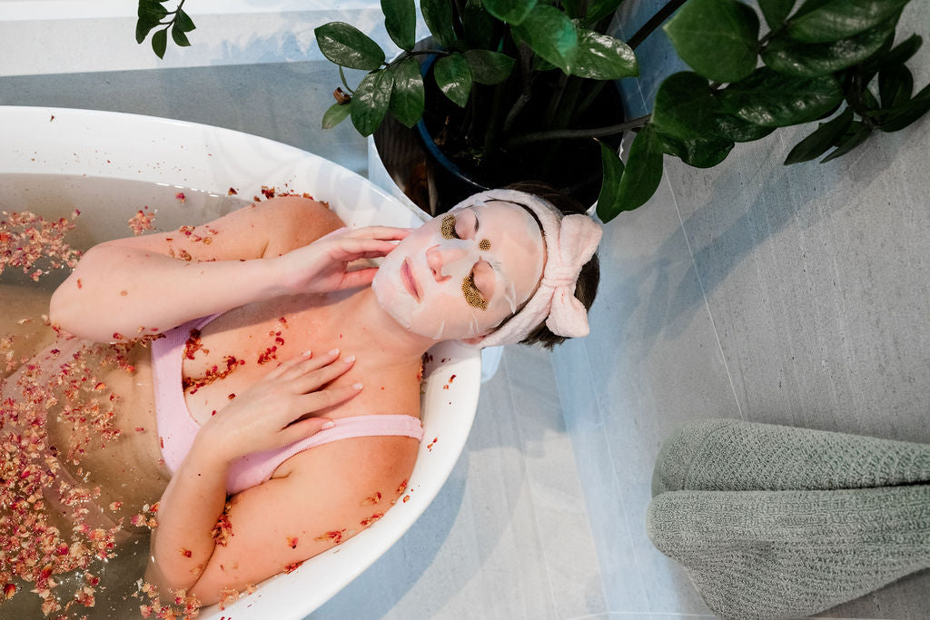 Person in a bathtub wearing Glo Younger Hydrating Sheet mask and QI Beauty Eye Lift Stims